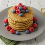 Fluffige Protein-Pancakes mit frischen Beeren und Ahornsirup auf einem weißen Teller